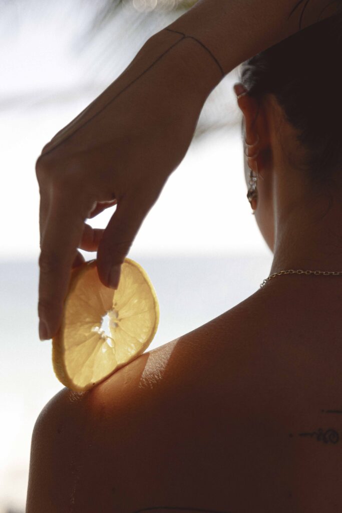 a girl holding a slice of orange in her hand looking at a sunrise in tulum beach, umi luxury boutique hotel